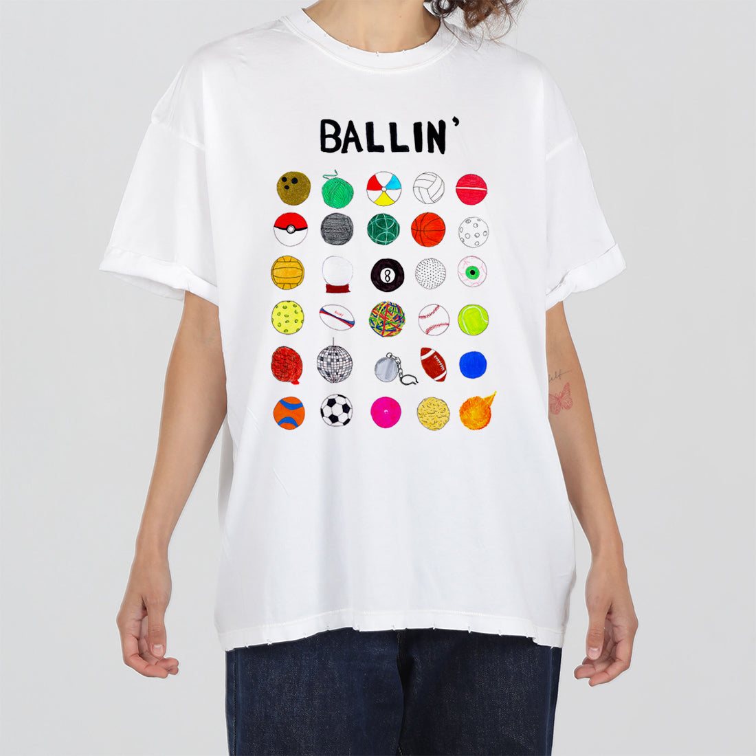 A person wearing a white t-shirt featuring the word "ballin'" at the top, with multiple colorful icons of different balls and ball-shaped items below the text.