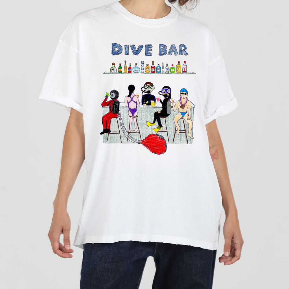 A person wearing a white t-shirt with a colorful graphic of five diverse women enjoying drinks at a bar labeled "dive bar." the design is playful and vibrant.