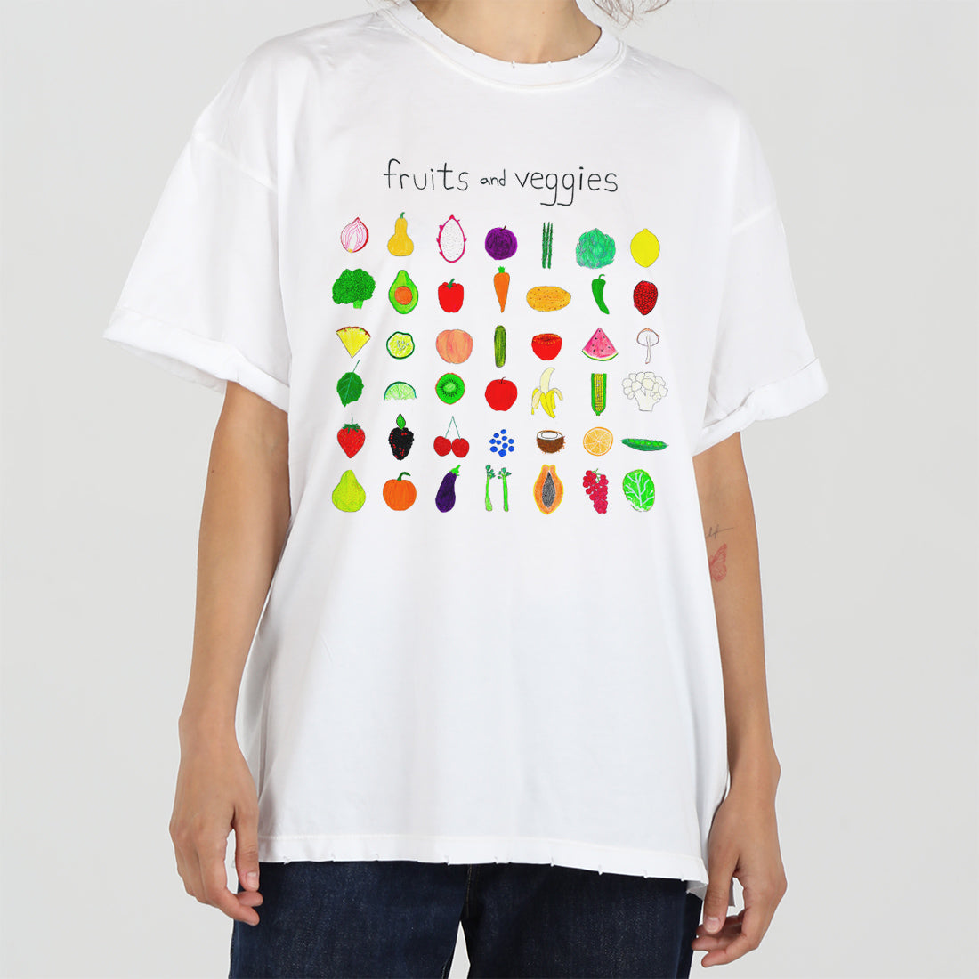 A person in a white t-shirt with colorful illustrations of various fruits and vegetables arranged in rows on the front, standing against a plain background.