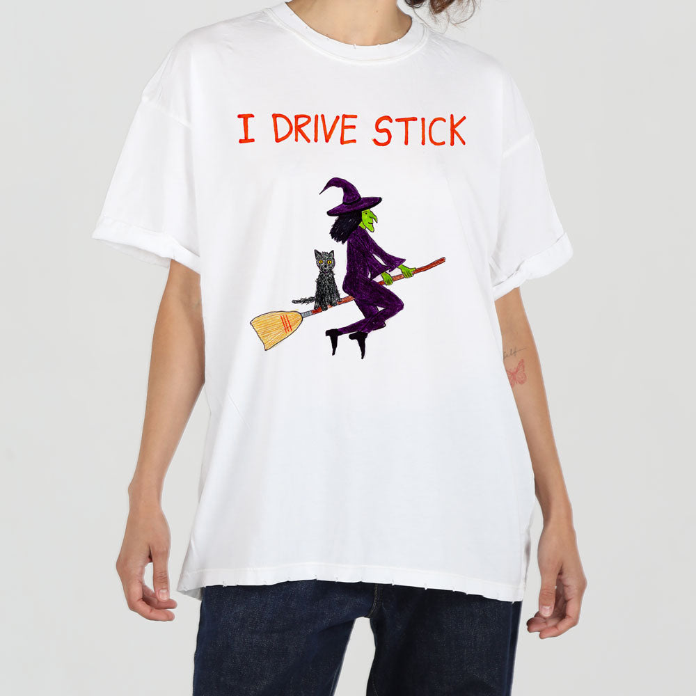 A person wearing a white t-shirt with the text "i drive stick" and a graphic of a witch riding a broomstick.