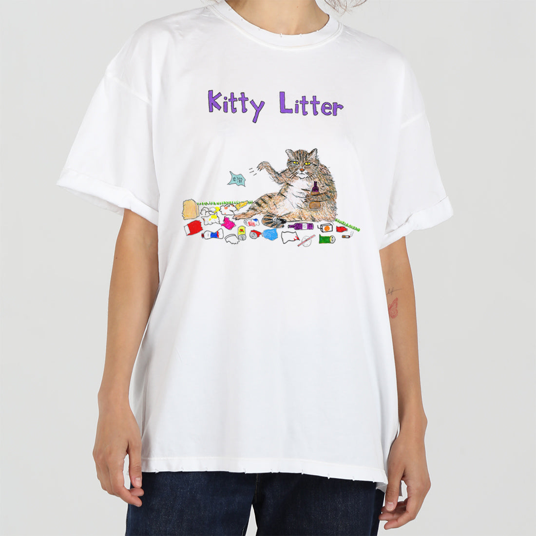 A person wearing a white t-shirt with a colorful graphic that reads "kitty litter" above an image of a cat sitting among various colorful trash items.