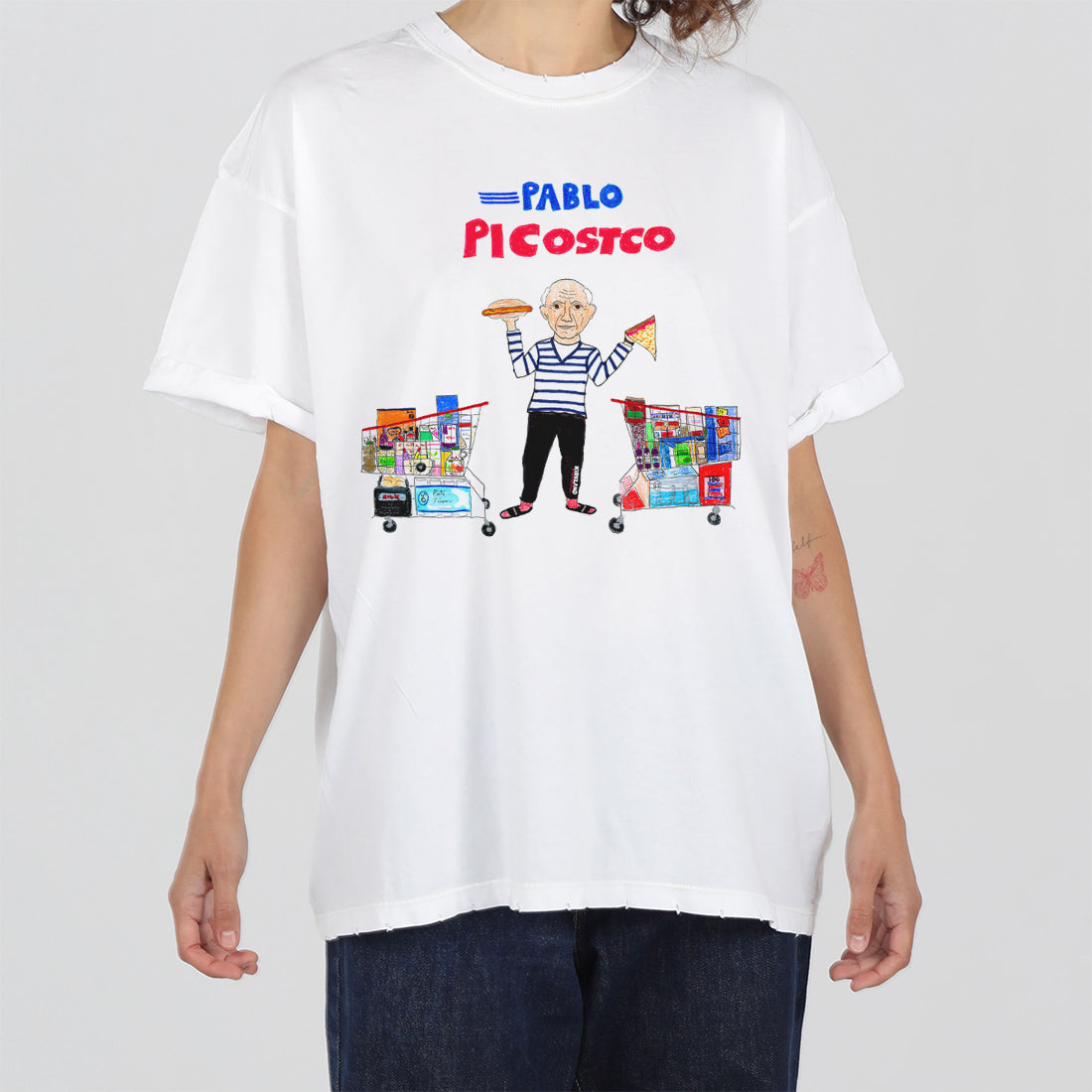 A person wearing a white t-shirt with a graphic design featuring an elderly man holding costco shopping carts filled with items, parodying pablo picasso with the text "pablo picostco" above.
