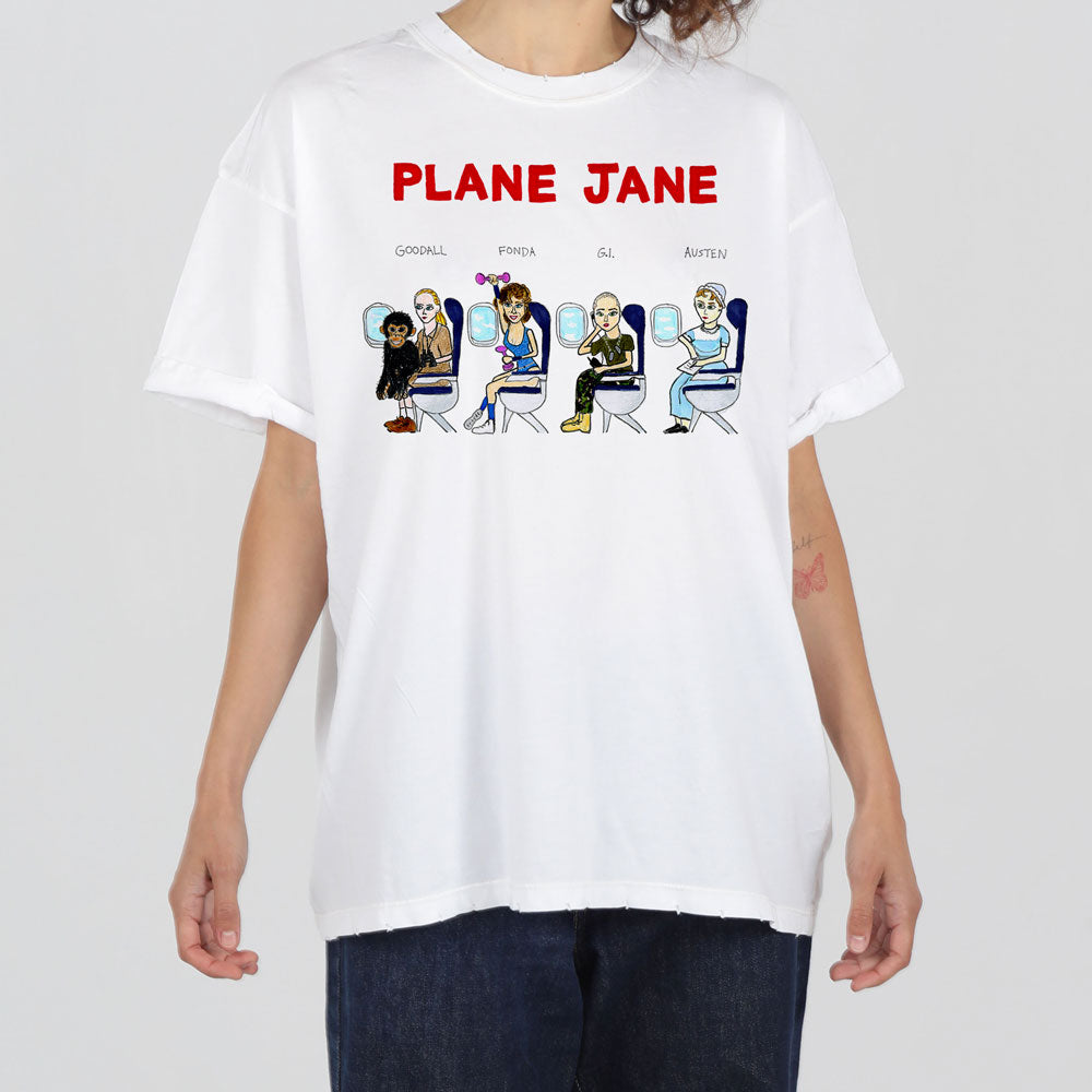 A person wearing a white t-shirt with a cartoon graphic of six diverse female characters seated in airplane seats, each labeled with different names like "goodall" and "frida.