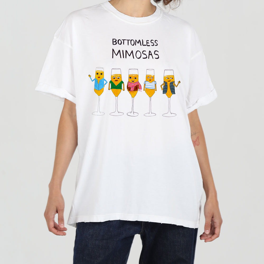 A person wearing a white t-shirt with a graphic of five anthropomorphic mimosa drinks in various colors, labeled "bottomless mimosas" above the glasses.