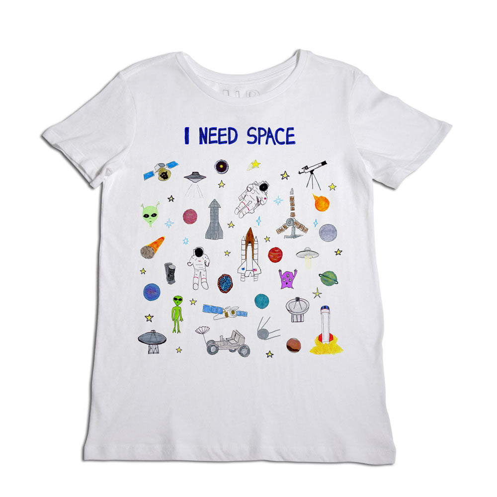 White t-shirt with a colorful space-themed design featuring the text "i need space," along with illustrations of astronauts, rockets, planets, and an alien.