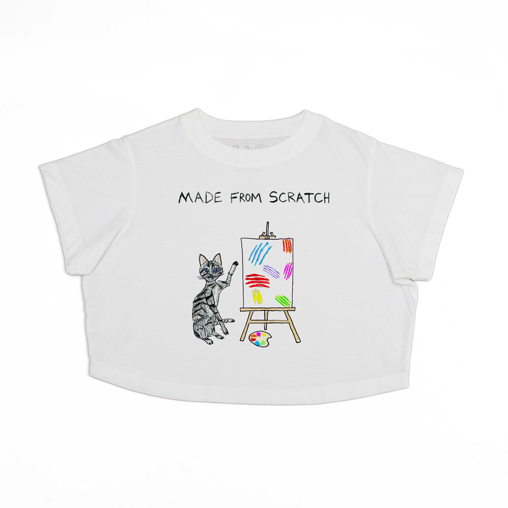 A white children's t-shirt with a drawing of a cat painting on an easel with colorful brushstrokes. Text above the drawing reads "MADE FROM SCRATCH.