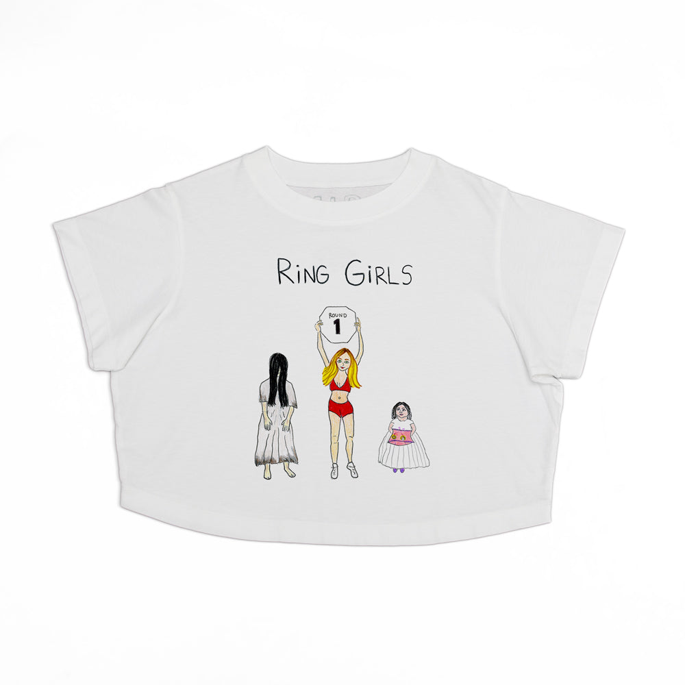 White cropped t-shirt featuring a graphic of three stylized women labeled "ring girls" standing under a sign with the number 1, illustrated in various outfits.