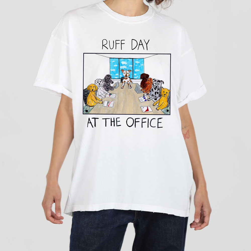 A person wearing a white t-shirt with a cartoon design of dogs in business attire sitting around a conference table, captioned "ruff day at the office.