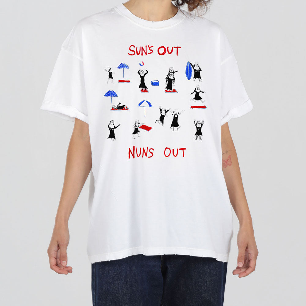 A person wearing a white t-shirt with a humorous graphic of dancing nuns and the phrase "sun's out nuns out" in red and black text.