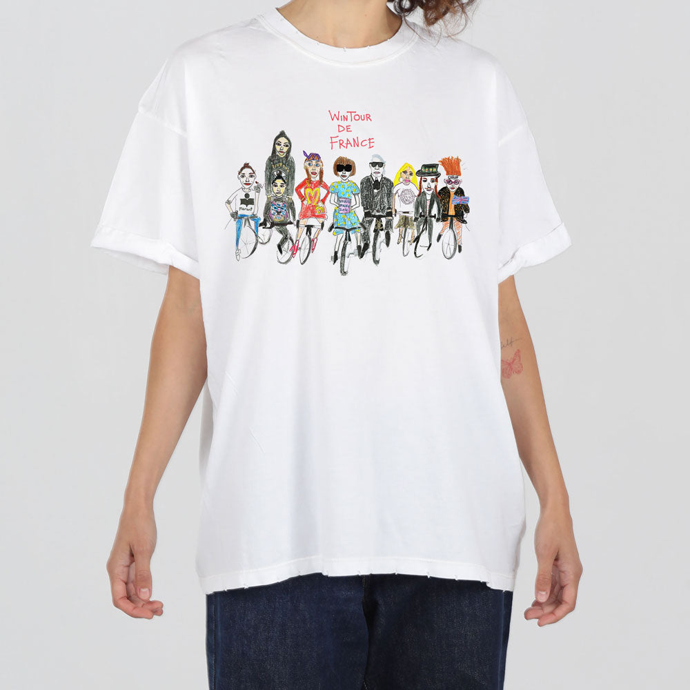 A person wearing a white t-shirt featuring colorful cartoon illustrations of cyclists competing in the tour de france. the design includes a text overlay that reads "le tour de france.