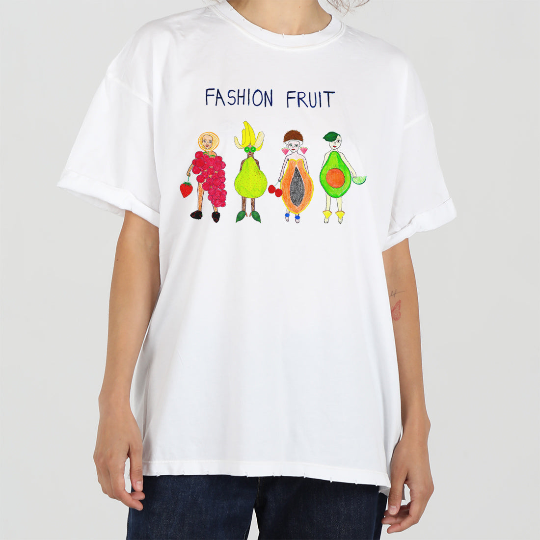 White t-shirt with "fashion fruit" text and cartoon fruit characters dressed stylishly, modeled by a person against a light background.