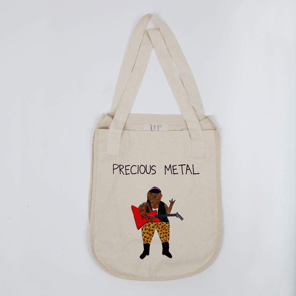 A beige tote bag featuring an illustration of a person playing a guitar with the phrase "precious metal" above. the figure wears a red shirt, black pants with spots, and a hat.