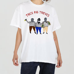 Person wearing a white T-shirt with an illustration of three figures dressed as thieves and the text "THICK ASS THIEVES" above them.