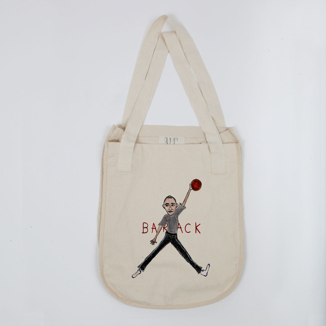 A beige canvas tote bag with a caricature of barack obama wearing a suit and holding a magnifying glass, with the word "barack" printed below.