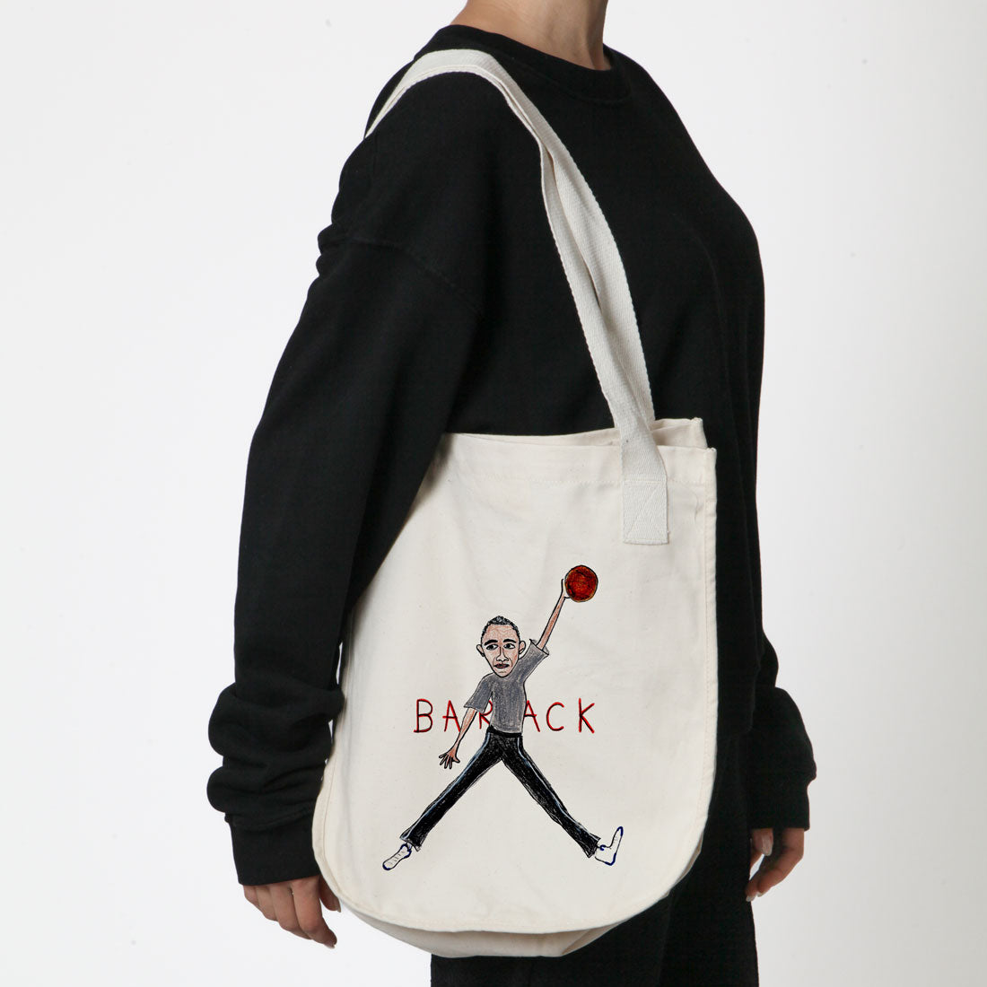 A person seen from the back, wearing a black long sleeve shirt and carrying a white tote bag with a graphic of a figure juggling an apple, and the word "balancing" written below it.
