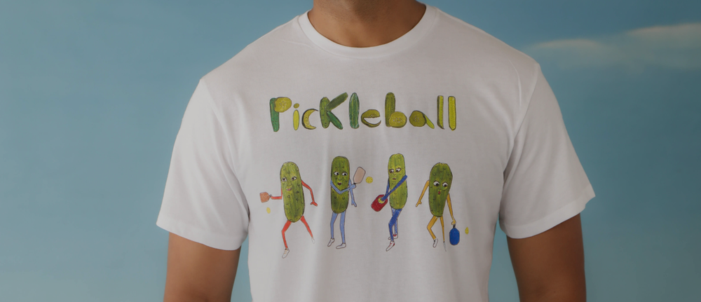 The torso of a black male model wearing a graphic t-shirt that says "Pickleball". 