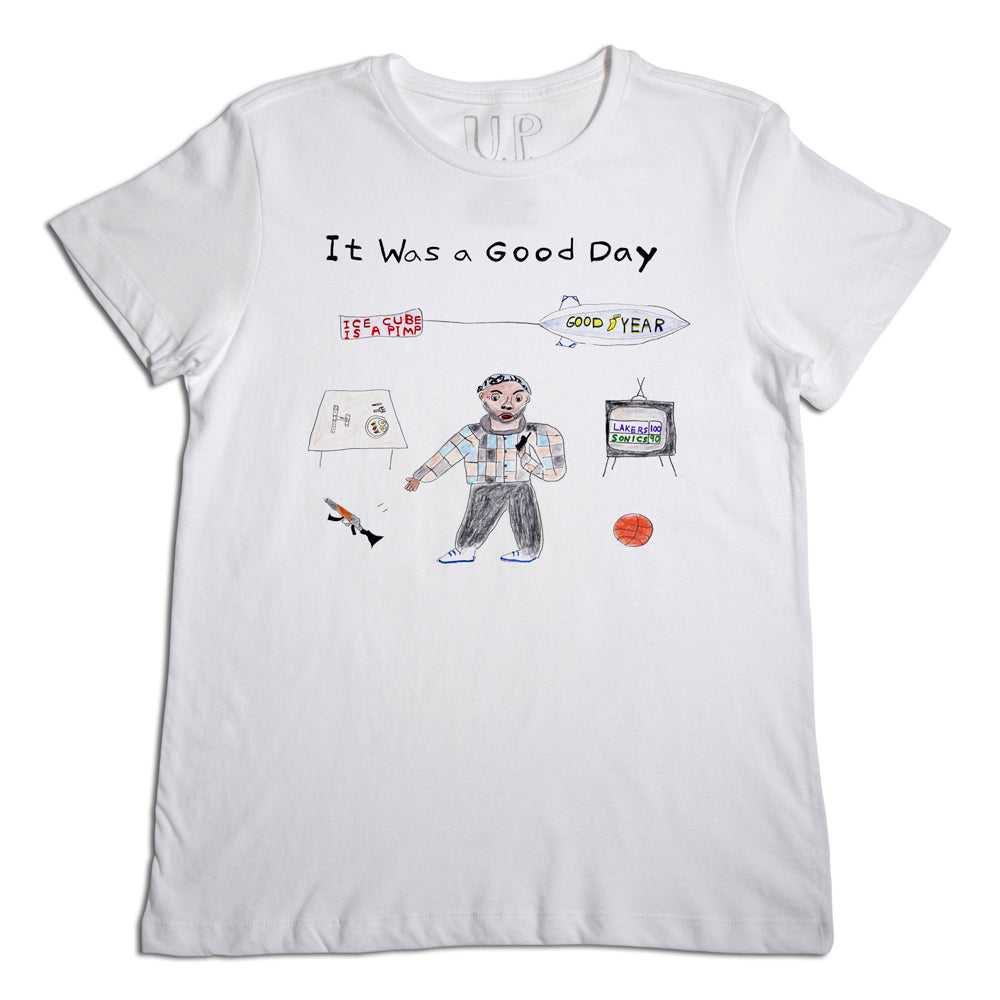 White t-shirt with a whimsical illustration featuring a doodled character in a plaid shirt and cap, surrounded by a fish, basketball, and other small sketches, with text "it was a good day" at the top.
