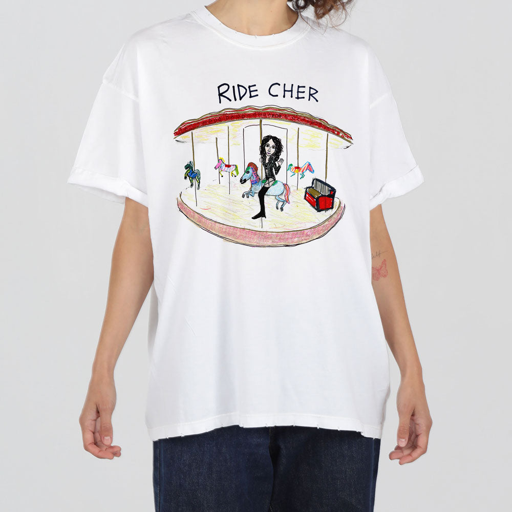 A person in a white t-shirt with a colorful graphic of a carousel featuring caricatured figures, including one on a horse. the text above the carousel reads "ride cher.