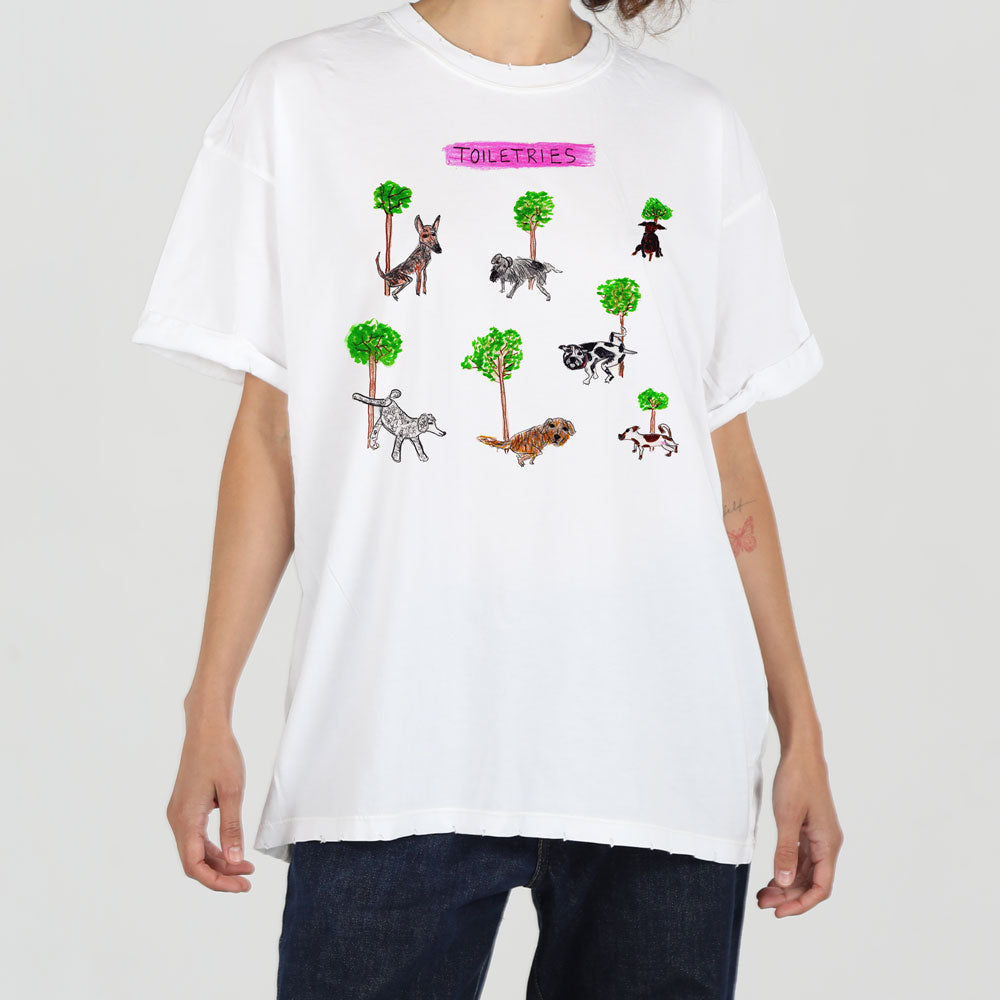 A person in a white t-shirt featuring a whimsical print of various animals and trees with the word "toiletries" in pink at the top.