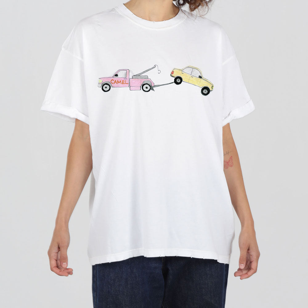 A person wearing a white t-shirt featuring a graphic of a pink tow truck towing a yellow car, standing against a neutral background.