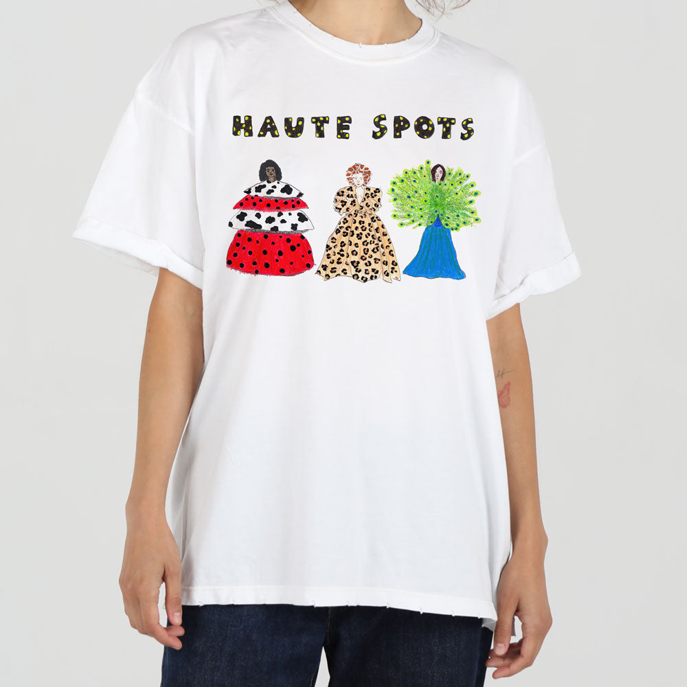 A person wearing a white t-shirt with the phrase "haute spots" and colorful peacock illustrations wearing fashionable dresses in red, patterned, and blue designs.