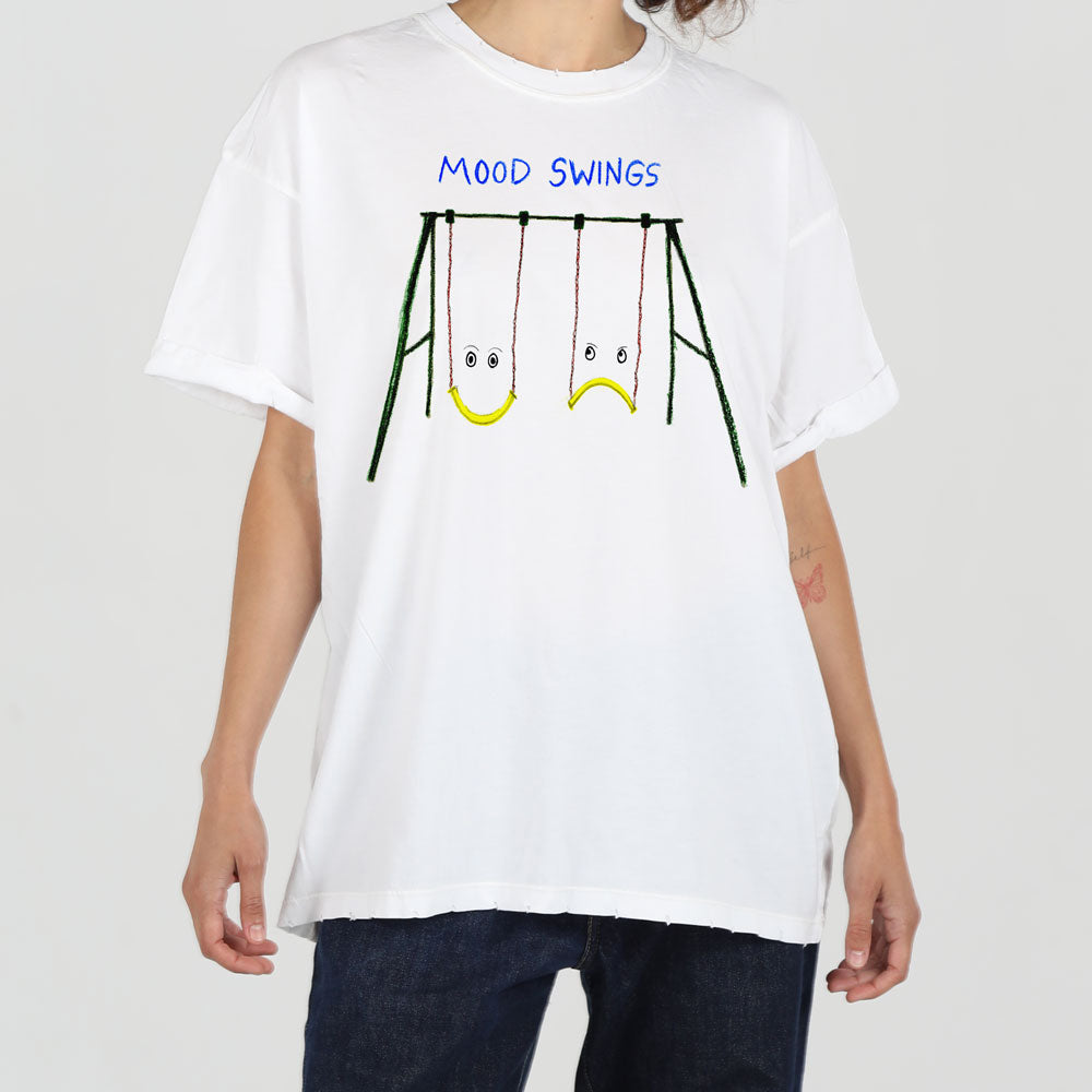A person wearing a white t-shirt with a graphic of three swings, each seat having a facial expression, and text above that reads "mood swings".