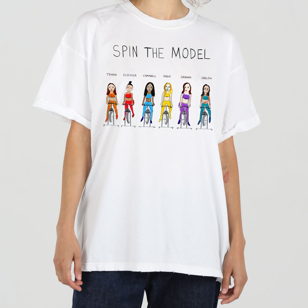 A person wearing a white oversized t-shirt featuring a graphic with eight stylized female models in various colorful outfits, labeled with names like tinson, ellesse, and carmel. the caption reads "spin the model.