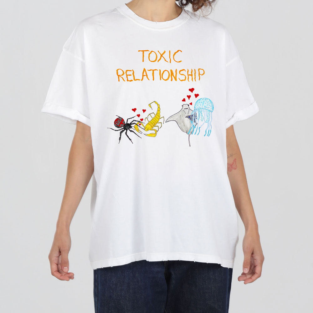 A person wearing a white t-shirt with the words "toxic relationship" and illustrations of a bee, a banana with wings, and a blue broken heart.